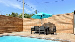 A swimming pool with a wooden fence, a table with chairs, and a blue umbrella. - The Oasis Private Pool Home + Best Launch Views! No cleaning fee. (Titusville)