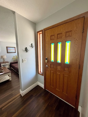 Une porte en bois ornée de vitraux, un mur blanc avec un tableau, et un plancher en bois.