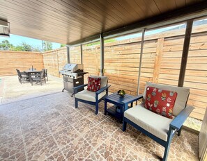 Une terrasse extérieure équipée d’un barbecue, d’un espace salon et offrant une vue sur le jardin arrière.