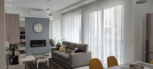 A modern living room with a grey sofa, a flat-screen TV, and a dining area with a table and chairs. - Bright Stylish Apartment in Victoria (Victoria)