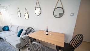 A modern living room with a sofa, chairs, a wooden table, and wall-mounted mirrors. - YalaRent Sunora 3BR APT - Families only (Eilat)