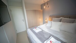 A neatly made bed with a white duvet and pillows, a bedside table with a lamp, and a wardrobe with sliding doors. - YalaRent Sunora 3BR APT - Families only (Eilat)
