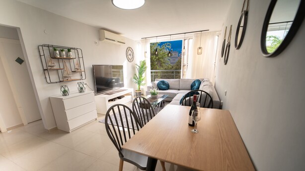 A modern kitchen with a dining area, a TV, and a large window with a view. - YalaRent Sunora 3BR APT - Families only (Eilat)