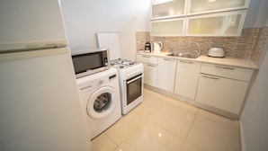 A compact kitchen with a washing machine, microwave, stove, and a coffee maker. - YalaRent Sunora 3BR APT - Families only (Eilat)