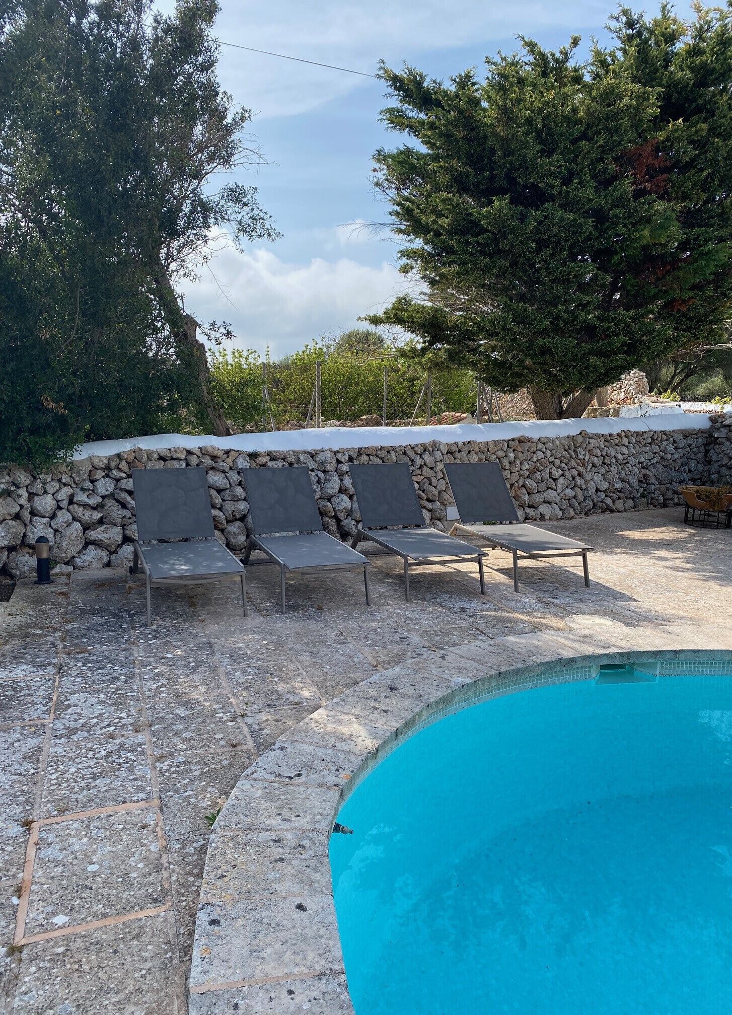 A swimming pool with three lounge chairs and a stone wall.