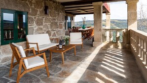A stone-floored balcony with wooden furniture, a table, and a vase with flowers.