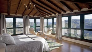 A bedroom with a large bed, two chairs, and a view of the mountains through large windows.