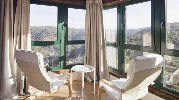 A room with two white chairs, a small round table, and large windows offering a view of a hilly landscape.