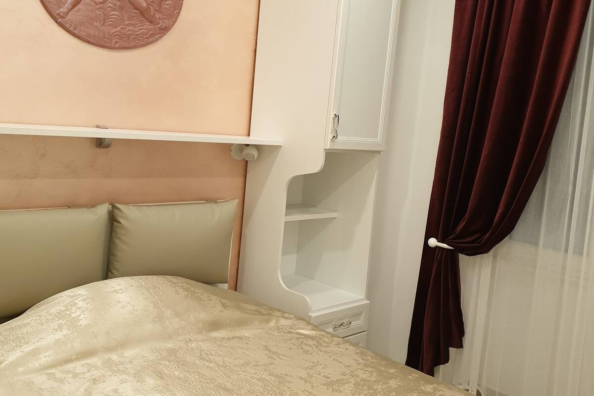 A bedroom with a bed, a headboard, a wall-mounted cabinet, and a window with curtains.