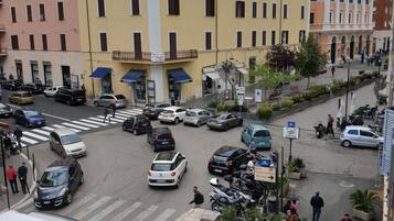 Una calle urbana concurrida, con coches aparcados y un autobús. Se ven edificios de varios pisos y balcones.