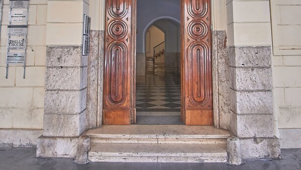 Entrada de un edificio con puertas de madera doble, una pared de piedra y una placa con número.