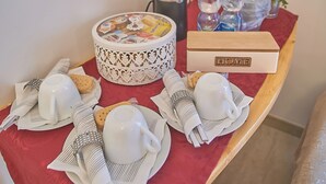 Una mesa de desayuno ordenada con mantel rojo, un cuenco decorativo, platos, tazas y una caja con la etiqueta 'HOME'.