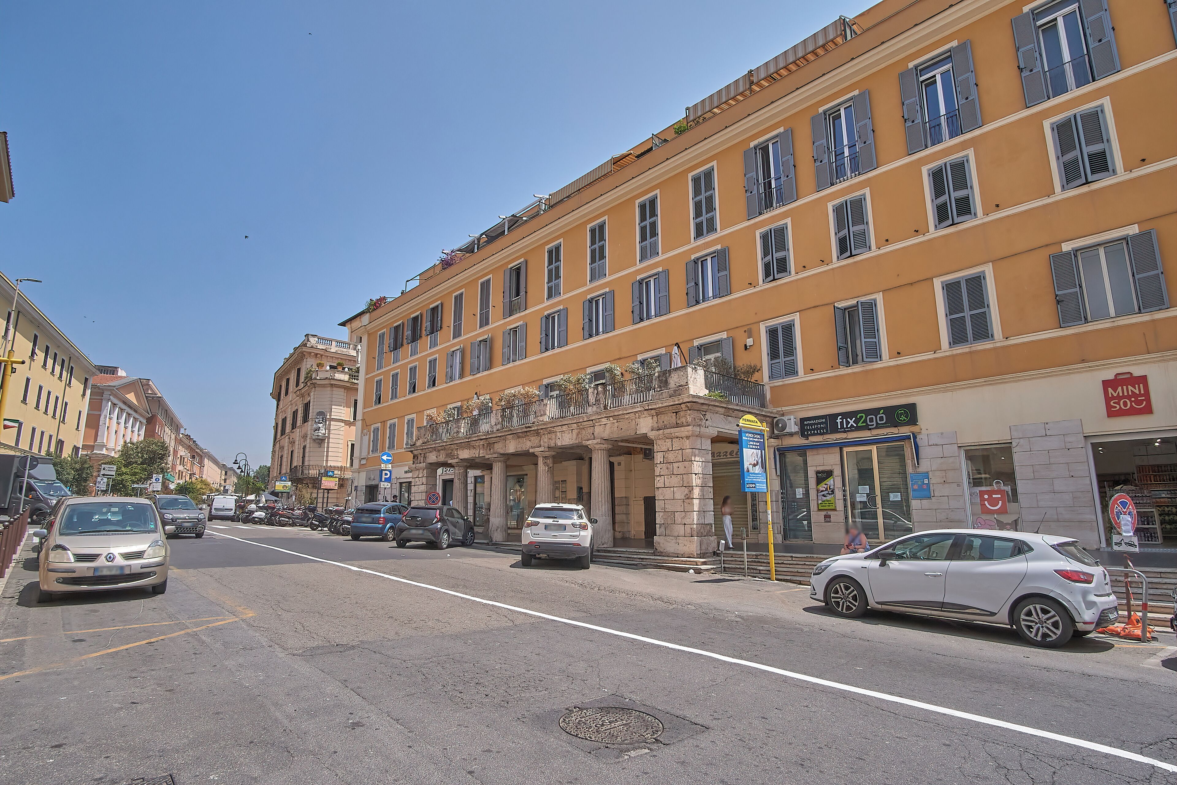 A street view with a building featuring a classical facade, a storefront with a sign, and parked cars.