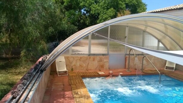 A swimming pool with a glass enclosure, surrounded by a patio area with a chair and a small table. - My holiday refuge in the Northeast of Mallorca (Font de Sa Cala)