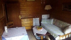 A cozy cabin room with a wooden interior, a bed, a table with a floral tablecloth, and a lamp. - My holiday refuge in the Northeast of Mallorca (Font de Sa Cala)