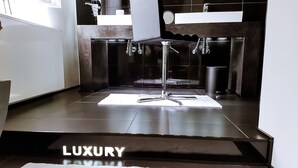 A modern bathroom with a large mirror, chrome fixtures, and a 'LUXURY' sign on the floor.