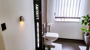 A modern bathroom with a toilet, a wall-mounted bidet, and a window with blinds.