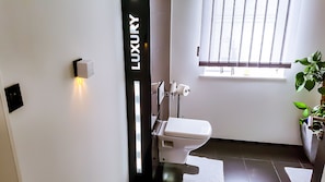 Een moderne badkamer met toilet, wandcloset en raam met zonwering.