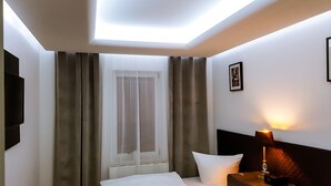 A hotel room with a bed, a nightstand with a lamp, a TV, and a window with curtains.