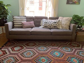 A living room with a brown sofa, patterned cushions, and a large geometric rug.