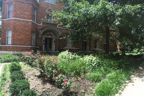 A brick building with a central entrance, surrounded by a well-maintained garden with various plants and flowers.