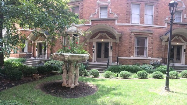 A brick building with a central fountain, surrounded by well-maintained lawns and hedges.