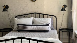A bed with a black metal frame, white bedding, and striped pillows. There are two black lamps on either side of the bed.