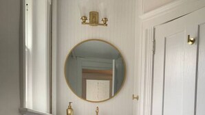 A narrow hallway with a dark wooden vanity, a round mirror, and a white door.
