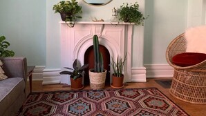A living room with a fireplace, a round mirror, and various potted plants.