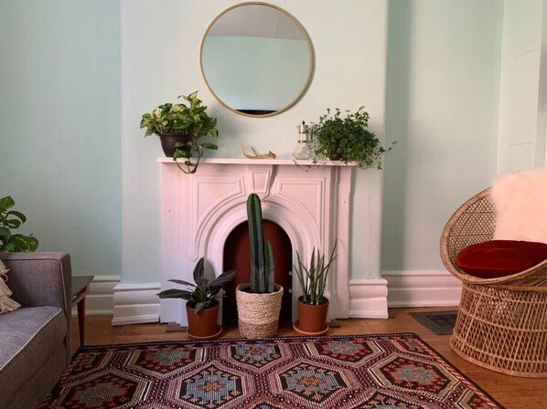 A living room with a fireplace, a round mirror, and various potted plants.