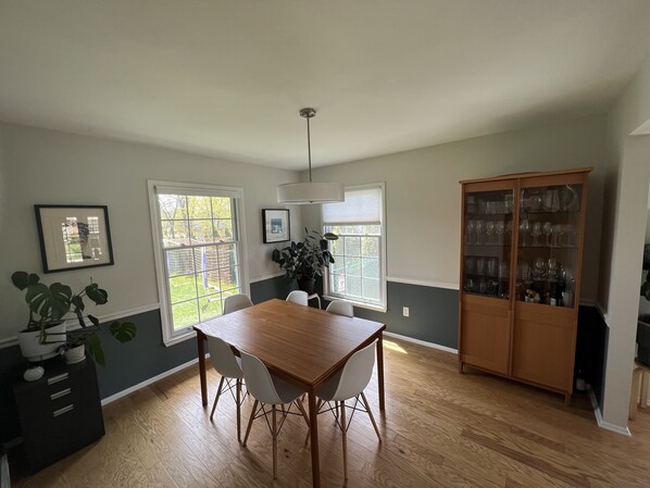 Un comedor con una mesa y sillas de madera, un armario con cristalería y ventanas grandes con vistas al exterior.