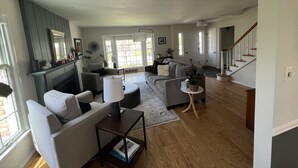 A spacious living room with a fireplace, a staircase, and a view of the outdoors. - Fantastic 4-Bedroom Family Home - Short Walk to Michigan Stadium (Ann Arbor)