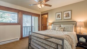 A bedroom with a bed, a ceiling fan, two framed pictures on the wall, and a nightstand with a lamp.