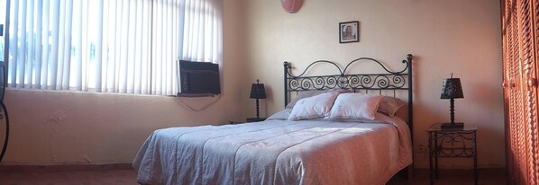 A bedroom with a bed, a nightstand, a lamp, a picture on the wall, and a window with blinds. - Beautiful villa with excellent location in complex with 2 pools (Ixtapa Zihuatanejo)