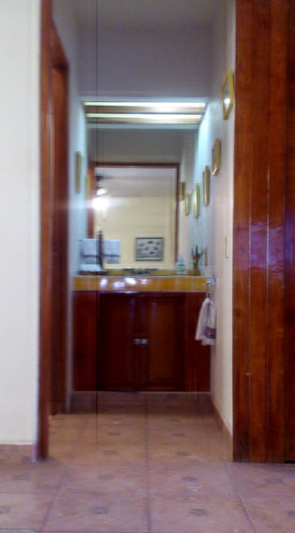 A narrow hallway leading to a room with a wooden door, a counter with a sink, and a mirror. - Beautiful villa with excellent location in complex with 2 pools (Ixtapa Zihuatanejo)