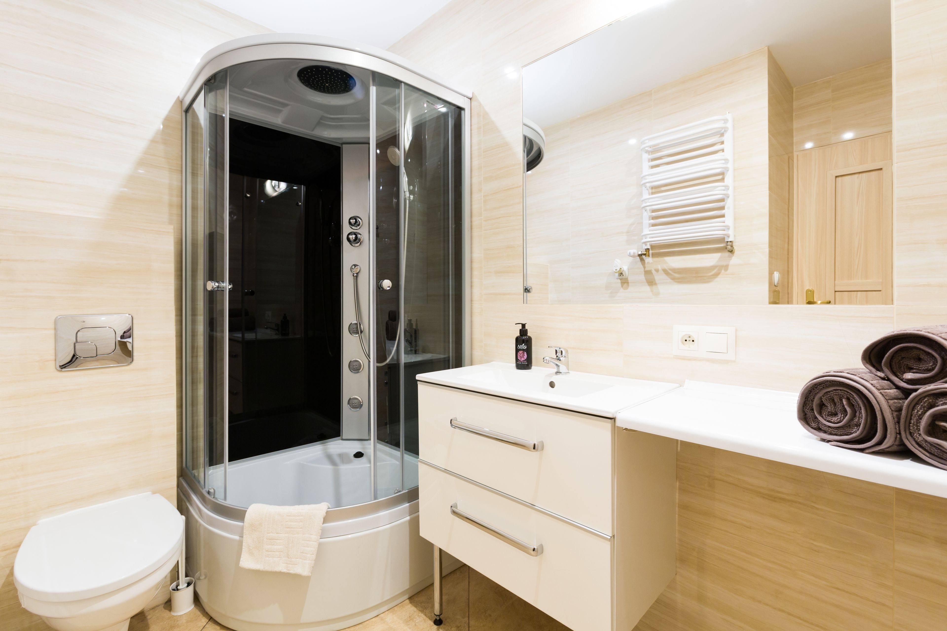 A modern bathroom with a glass-enclosed shower, a white toilet, a vanity with a mirror, and a towel rack.
