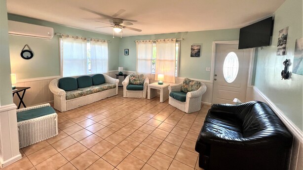 A living room with a ceiling fan, two white wicker sofas with teal cushions, a black leather couch, and a small table with a lamp.