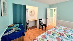 A bedroom with a bed, a desk, a chair, a ceiling fan, and a door leading to another room.