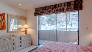 A bedroom with a large bed, a dresser with drawers, a mirror, and a window with a view of a snowy outdoor area. - Sawtooth Condo 25 - Your Nest in the Mountains with Hot Tub Onsite (Ketchum)