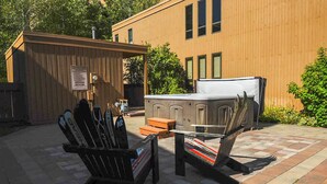 A wooden building with a small outdoor seating area, a hot tub, and skis leaning against a wall. - Sawtooth Condo 25 - Your Nest in the Mountains with Hot Tub Onsite (Ketchum)