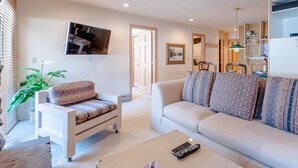 A living room with a sofa, armchair, and a coffee table with remotes. - Sawtooth Condo 25 - Your Nest in the Mountains with Hot Tub Onsite (Ketchum)