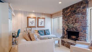 A living room with a stone fireplace, a white sofa, and two framed pictures on the wall. - Sawtooth Condo 25 - Your Nest in the Mountains with Hot Tub Onsite (Ketchum)