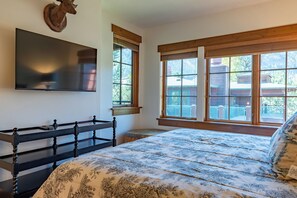 Ein Schlafzimmer mit einem Bett, einem an der Wand befestigten Fernseher, einem Holzkopfende und großen Fenstern mit Blick ins Freie.
