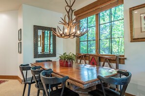 A dining area with a large wooden table, chairs, a chandelier, and large windows. - Westridge Condo 27 - Cozy Condo Convenient Locale to Downtown Ketchum (Ketchum)