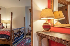 Una habitación con una cama, una silla de madera, una mesa con una lámpara y un espejo en la pared.
