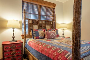 A bedroom with a wooden headboard, two bedside lamps, a red nightstand, and a quilted bedspread.
