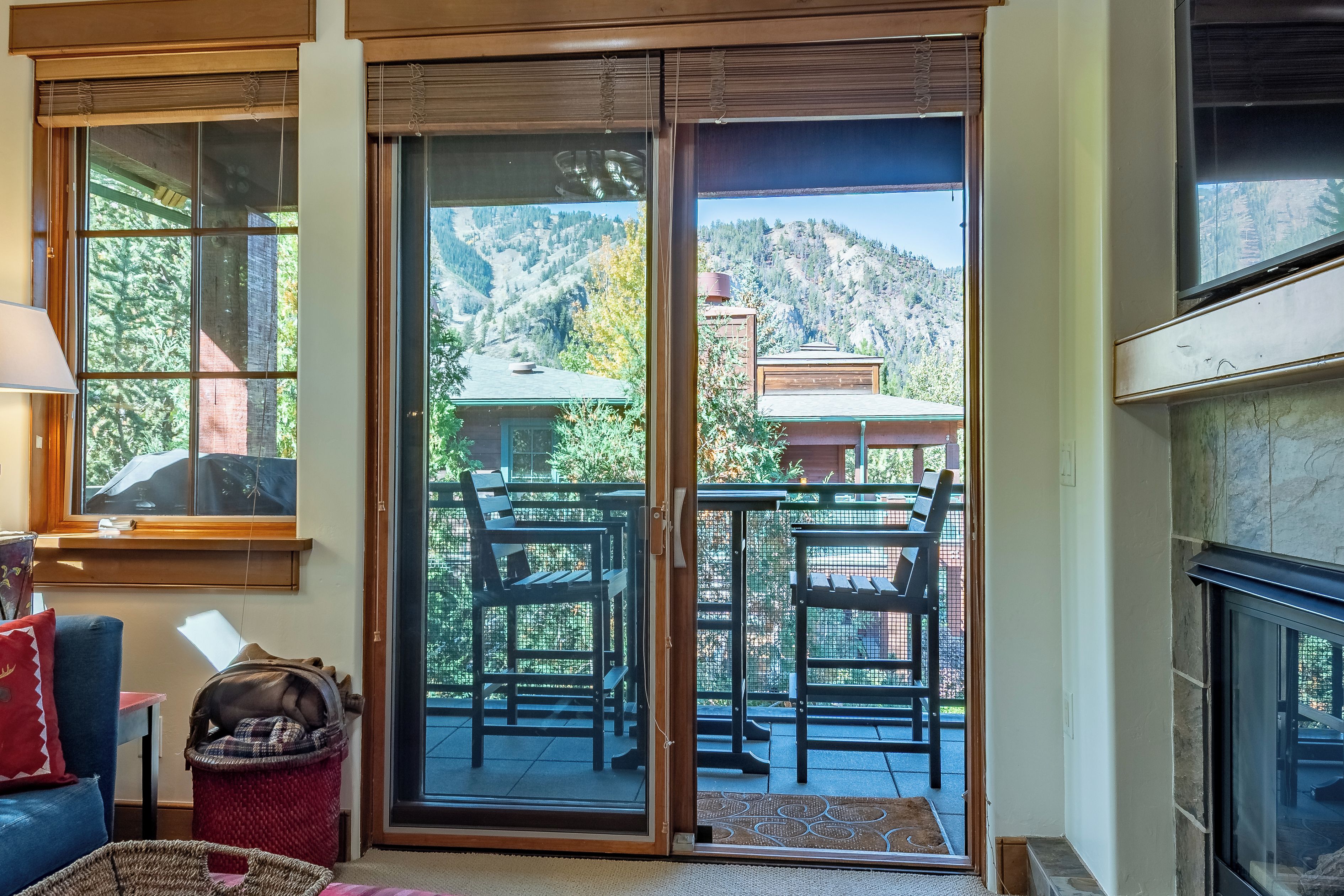 A room with a sliding glass door leading to an outdoor patio with a table and chairs, a fireplace, and a view of a mountainous landscape.