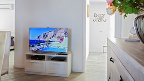 Un salon moderne avec un téléviseur à écran plat posé sur un meuble de télévision blanc, une commode en bois et une porte ornée d’une citation inspirante.