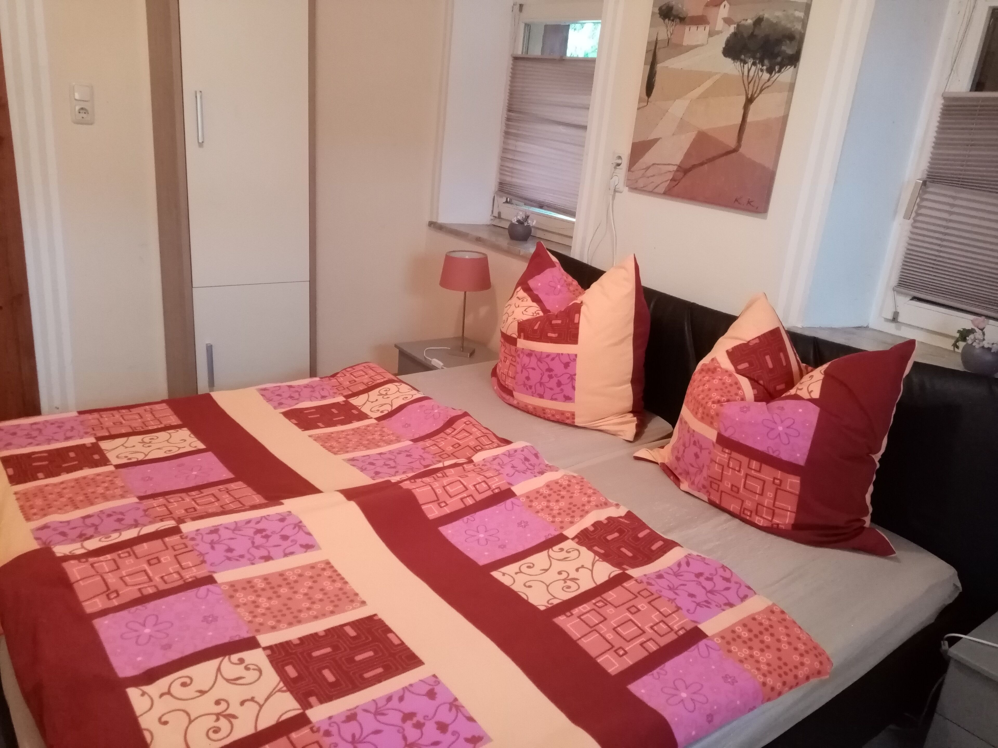 Ein Schlafzimmer mit einem Bett, Kissen, einem Nachttisch, einer Lampe und einem Bild an der Wand.