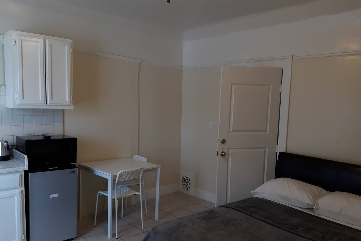 Ein kleines Zimmer mit Bett, Schreibtisch, Kühlschrank und Mikrowelle.